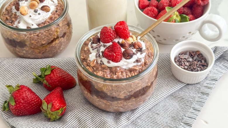 Chocolate overnight oats in glasses, topped with whipped cream and raspberries