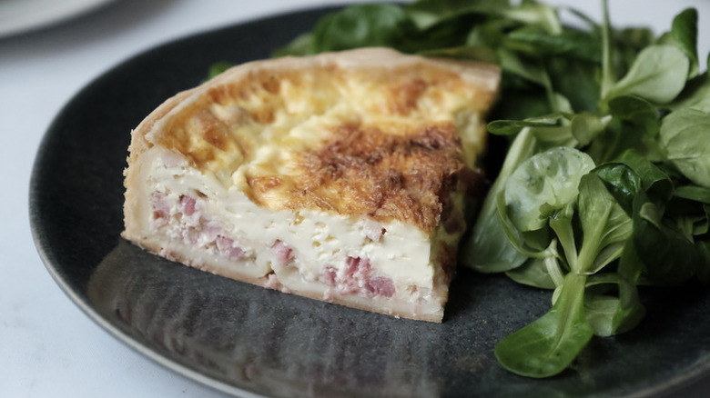 Slice of quiche Lorraine on plate with fresh spinach