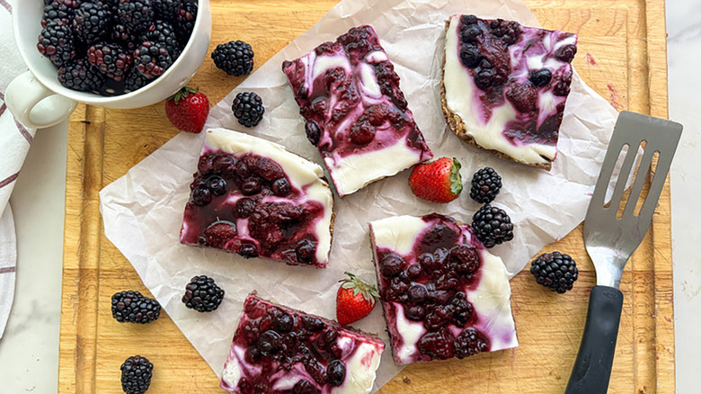 Yogurt and blackberry-topped granola bars on parchment-lined wooden board
