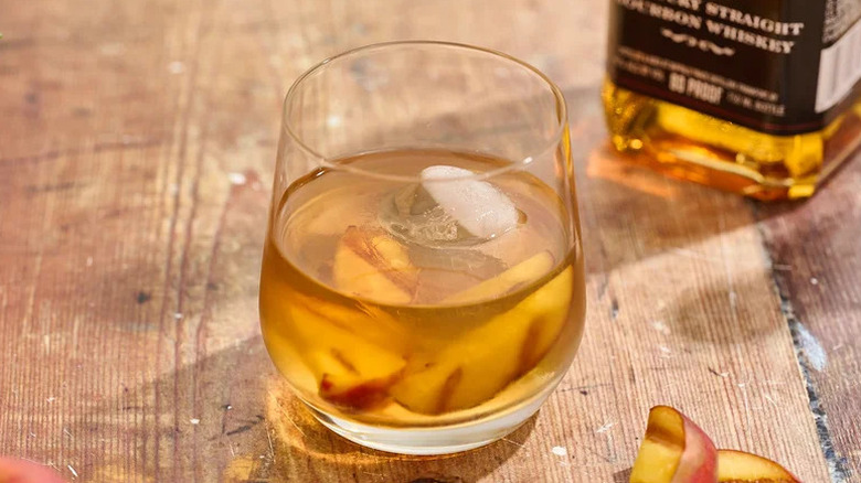Grilled Peach Old Fashioned in glass with ice on wooden table