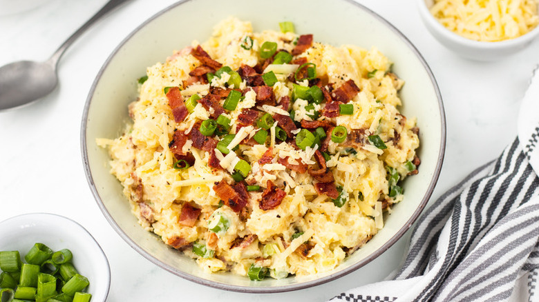 Baked potato salad in bowl, topped with bacon bits and chopped green onion