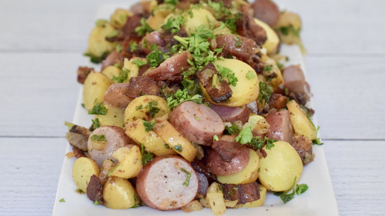 Potato and sausage salad piled onto white rectangular serving platter