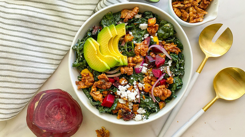 Kale salad in white bowl, topped with avocado slices and roasted walnuts