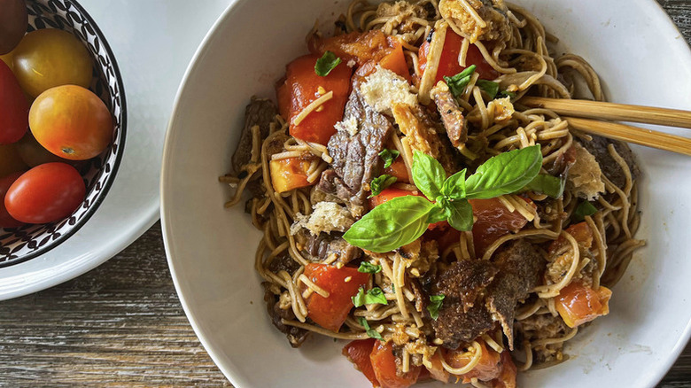 Beef and noodles salad in white bowl with chopsticks