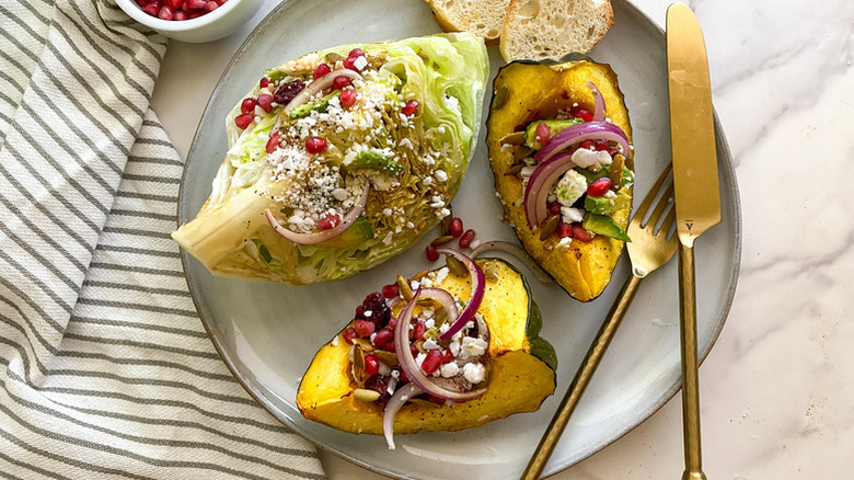 Roasted acorn squash wedge salad on plate, topped with pomegranate seeds and red onion slices