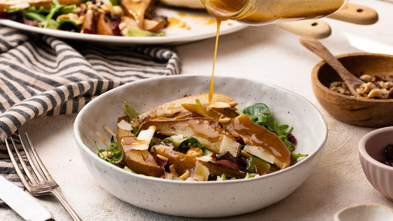 Pouring dressing onto bowl of roasted pear and Manchego salad