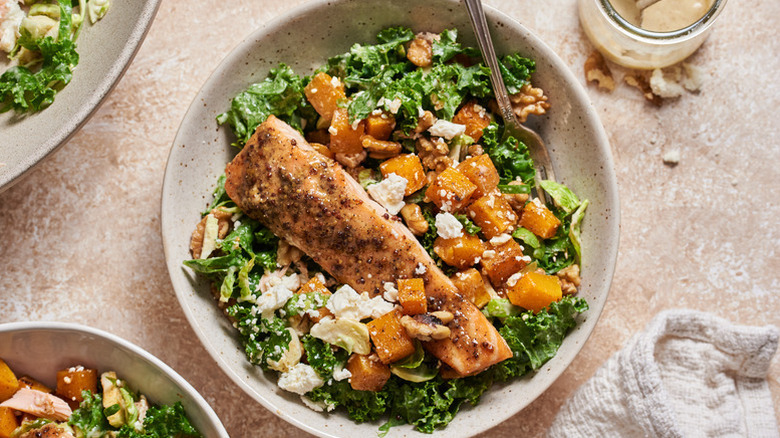 Salmon, roasted squash, and kale salad in bowl with fork