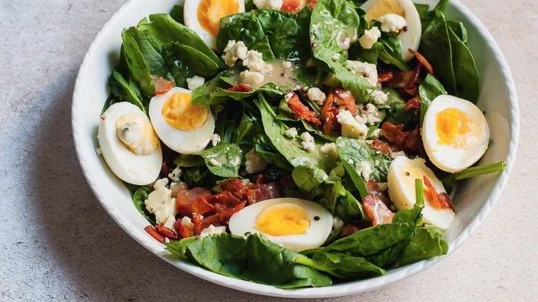 Spinach salad in white bowl, topped with halved hard boiled eggs