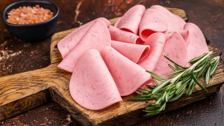 Sliced deli meat on wooden cutting board with sprig of rosemary