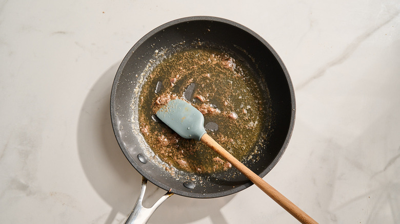 skillet with melted anchovies cooling on counter