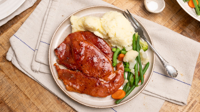brown sugar ham steak on plate with vegetables and mashed potatoes