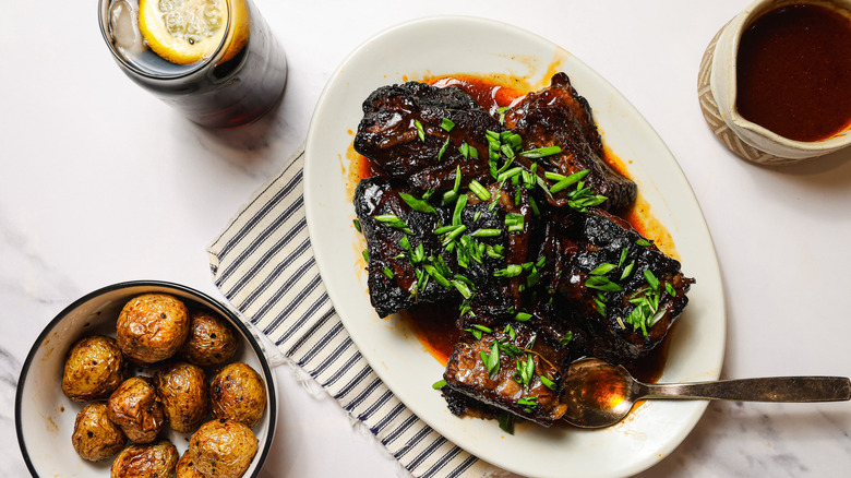 Slow cooker short ribs on platter with potatoes and sauce besides