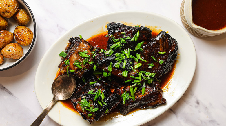 Slow cooker short ribs on platter with potatoes and sauce besides