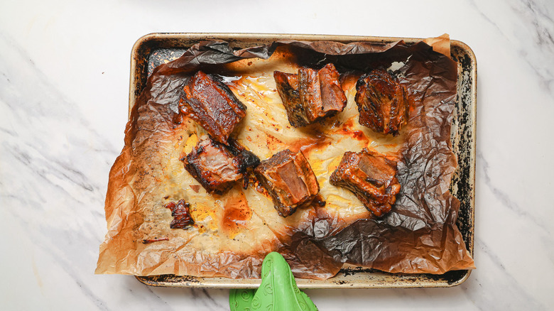 Hand holding baking sheet with broiled ribs