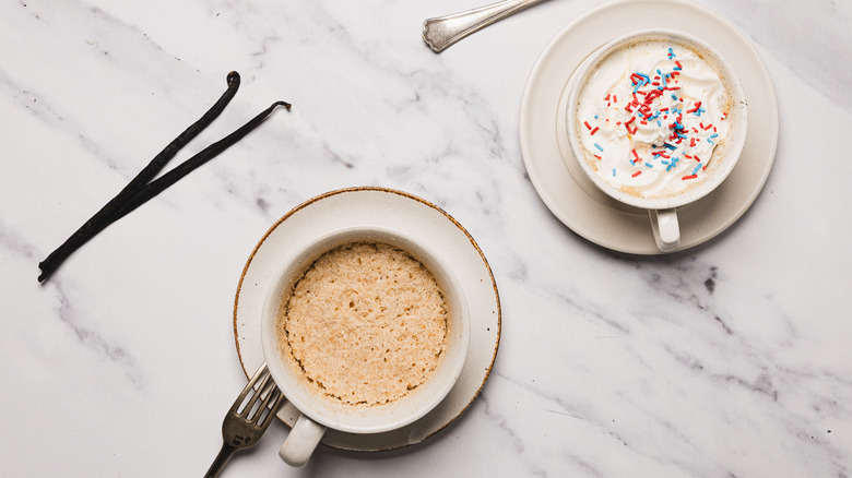 Two vanilla mug cakes, one plain and one with whipped cream and sprinkles