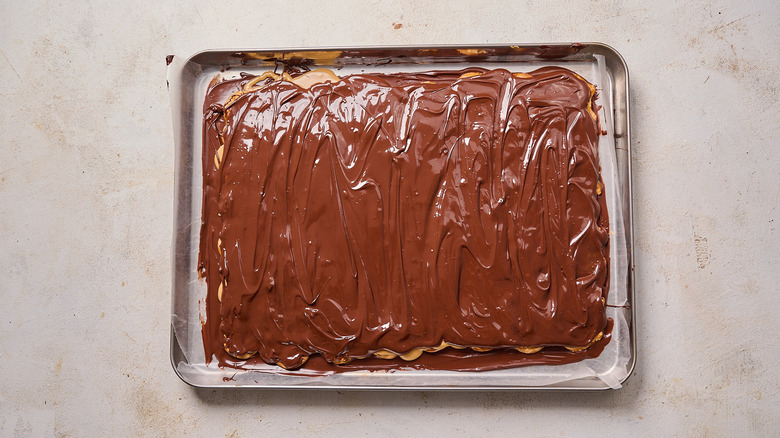 smoothing chocolate into a single layer on peanut butter