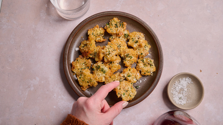 hand reaching for smashed tater tots on a plate