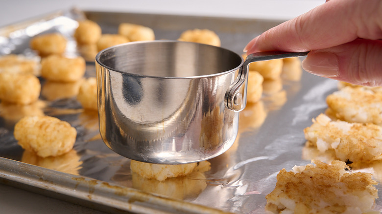 smashing tater tots with measuring cup