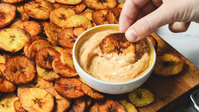 Hand dipping a plantain chip into sauce