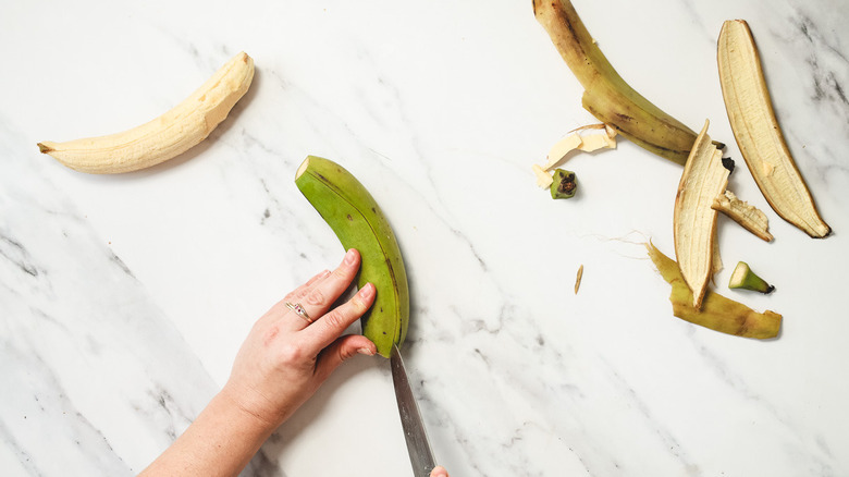 Slicing vertical slits in the peel of a green plantain