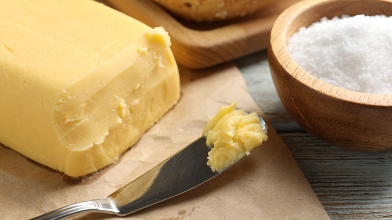 A stick of creamy, homemade butter with a knife holding a small pat next to a bowl of salt