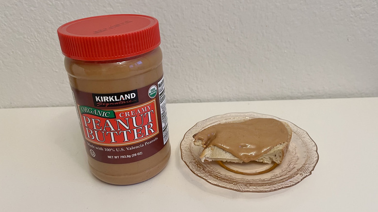 Jar of Kirkland Signature Organic Creamy Peanut Butter with piece of bread