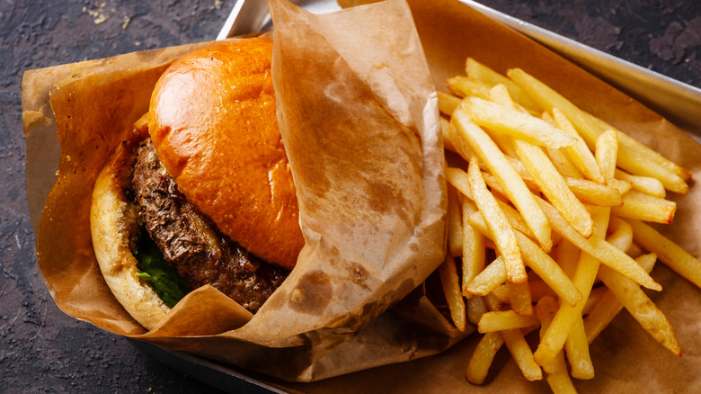 Paper-wrapped hamburger and fries on a paper-lined metal tray