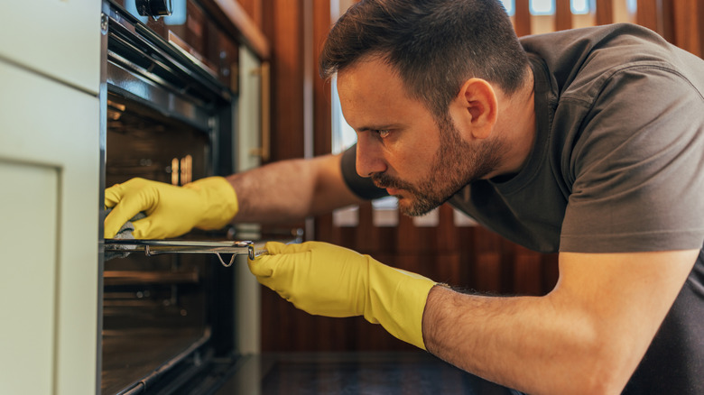 Man wearing yellow gloves, deep cleaning an oven