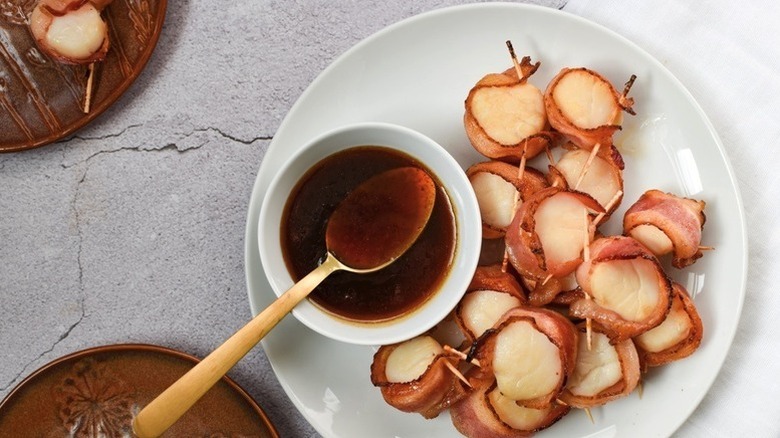 Bacon-wrapped scallops on skewers, served with bowl of apple cider sauce