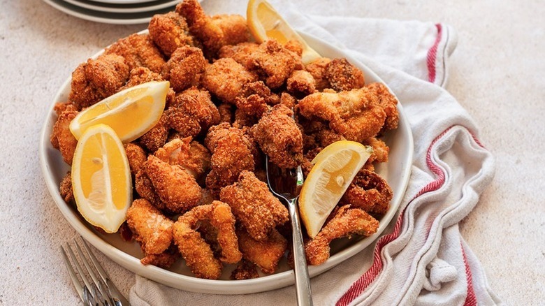 Pile of crispy catfish nuggets on plate with lemon wedges