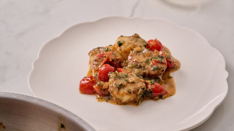 Buttery seared scallops and tomatoes on white plate