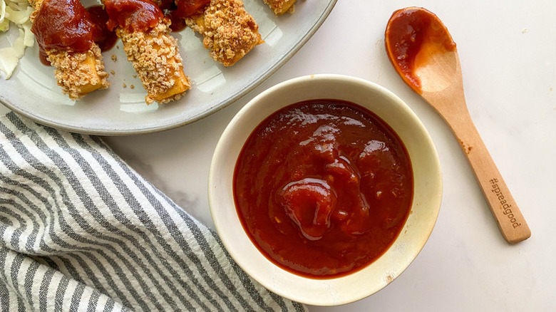 Bowl of tonkatsu sauce next to wooden spoon and plate of crispy tofu