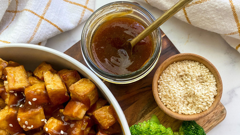 Bowl of teriyaki sauce next to bowls of sesame seeds and crispy tofu