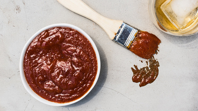 Bowl of bourbon-chile barbecue sauce next to sauce-covered brush