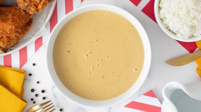 Bowl of creamy gravy next to bowl of rice and plate of fried chicken