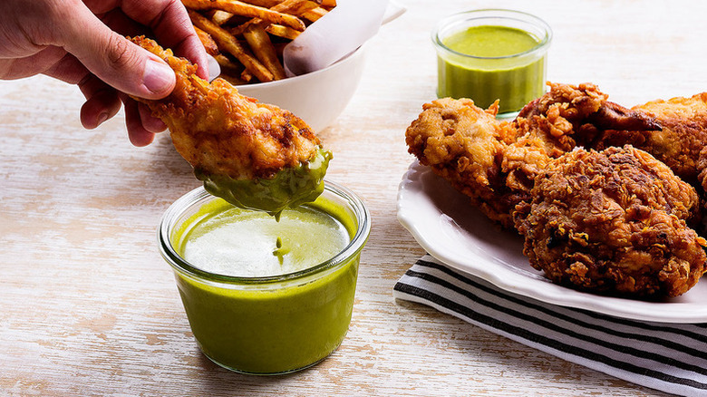 Hand dipping fried chicken into bowl of green herb sauce