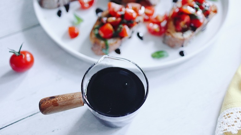 Balsamic glaze in small pouring jug next to plate of bruschetta