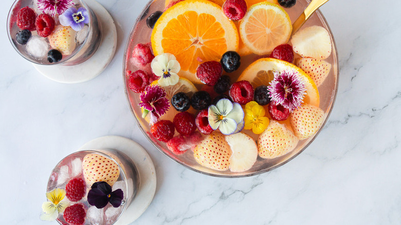 Fruity punch in bowl and glasses, with orange rounds, berries, and edible flowers