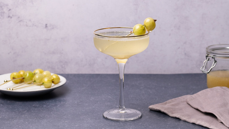 Gooseberry fizz cocktail in coupe glass, garnished with skewered candied gooseberries