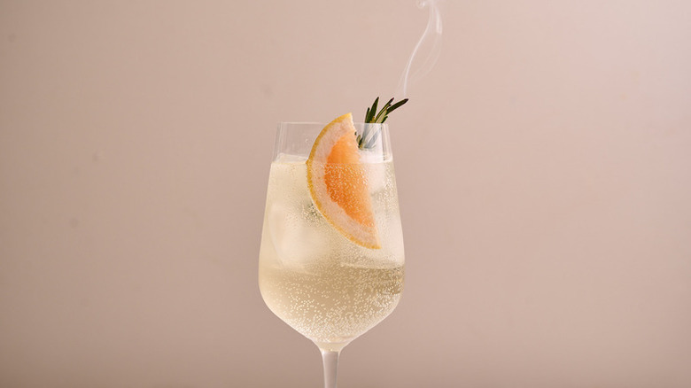 White wine spritzer in glass with grapefruit slice and smoking sprig of rosemary