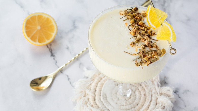 Creamy lemon cocktail in coupe glass, garnished with dried chamomile flowers and candied lemon