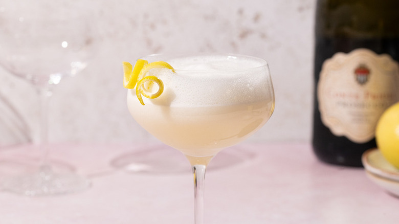 Pale peach-colored cocktail with a frothy top, garnished with a lemon twist