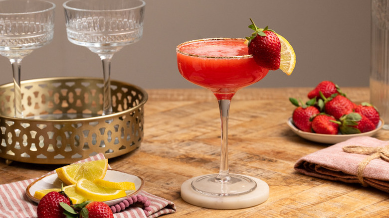 Strawberry and lemon cocktail in long-stemmed glass next to plates of fresh strawberries and lemon slices