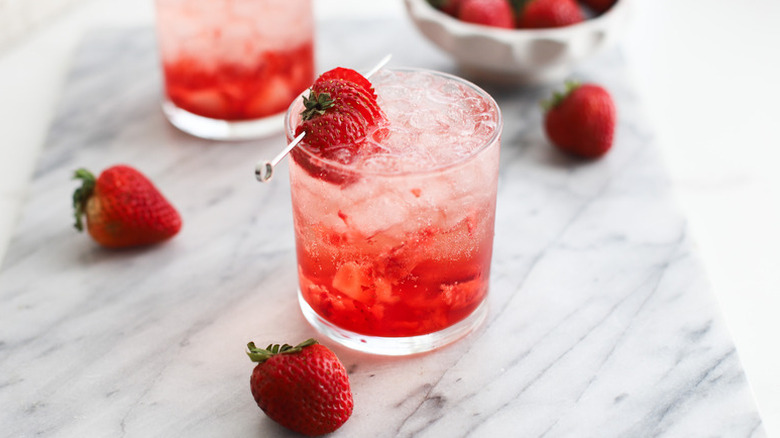 Strawberry cocktail in glass with crushed ice, garnished with skewered fresh strawberries