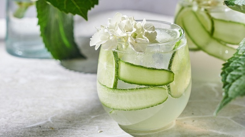 White linen cocktail garnished with cucumber ribbons, lime slices, and white edible flowers
