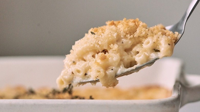 Spooning mac and cheese casserole from white baking dish