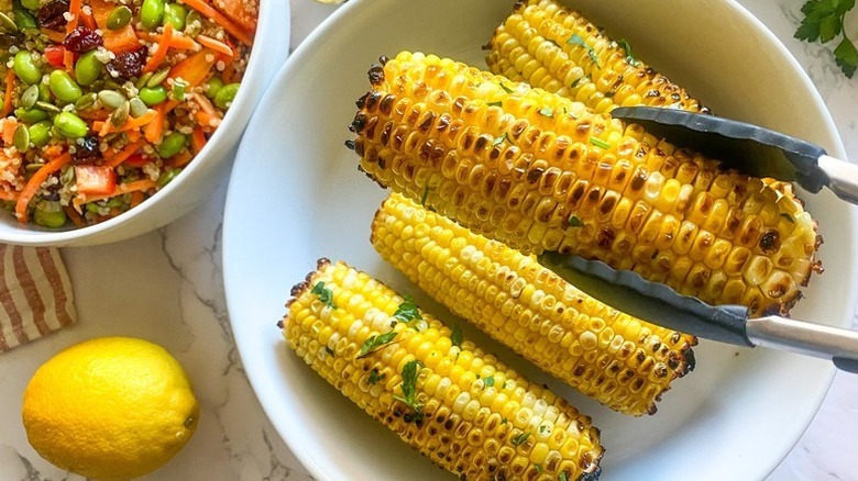 Lifting grilled corn on the cob from bowl with tongs