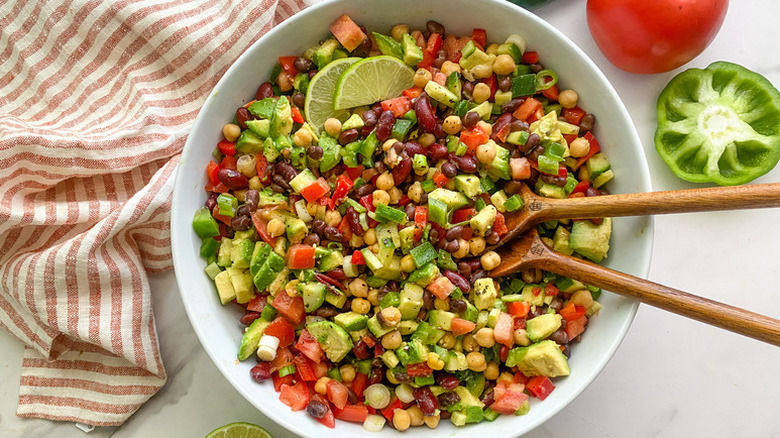 Three bean salad in bowl with wooden serving spoons and lime slices