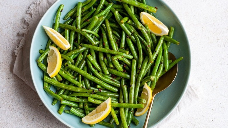 Sauteed green beans on blue plate with lemon wedges