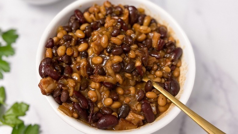 Slow cooker baked beans in white bowl with spoon